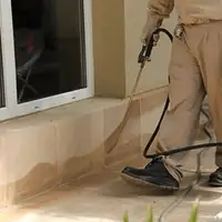 General pest control technician spraying exterior perimeter around a home in Dover, DE