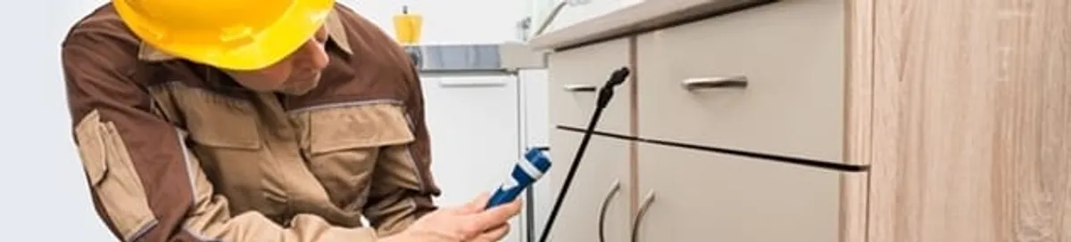 Roach exterminator applying treatment under kitchen cabinets in Dover, DE